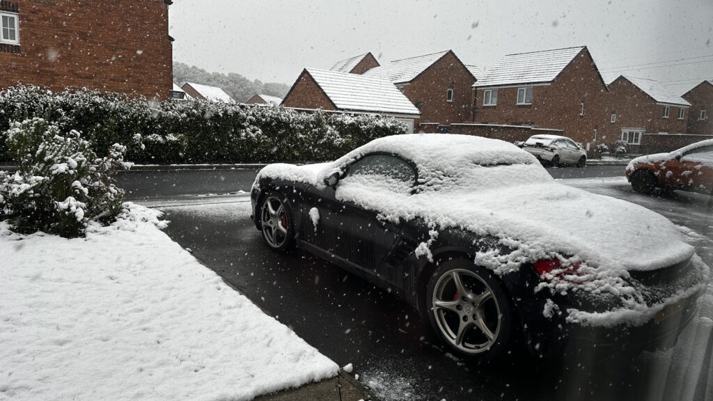 A photo of a sports car parked on a driveway, with the car and the area around it covered in a layer of snow.
